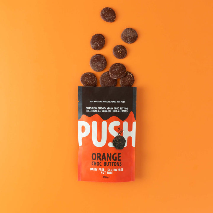 Push Chocolate Orange Dairy Free Chocolate Buttons pictured on an orange backdrop with dairy-free chocolate buttons coming out the top of the packaging.
