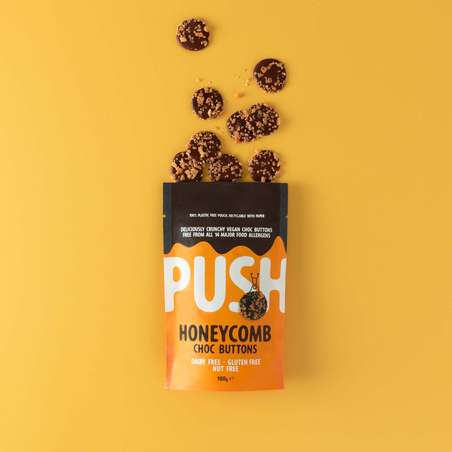 Push Chocolate Honeycomb Chocolate Buttons pictured on a yellow backdrop with dairy-free chocolate buttons coming out the top of the packaging.