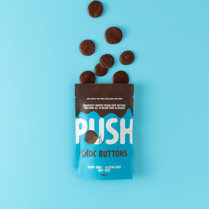 Push Chocolate Original Chocolate Buttons pictured on a blue backdrop with dairy-free chocolate buttons coming out the top of the packaging. 