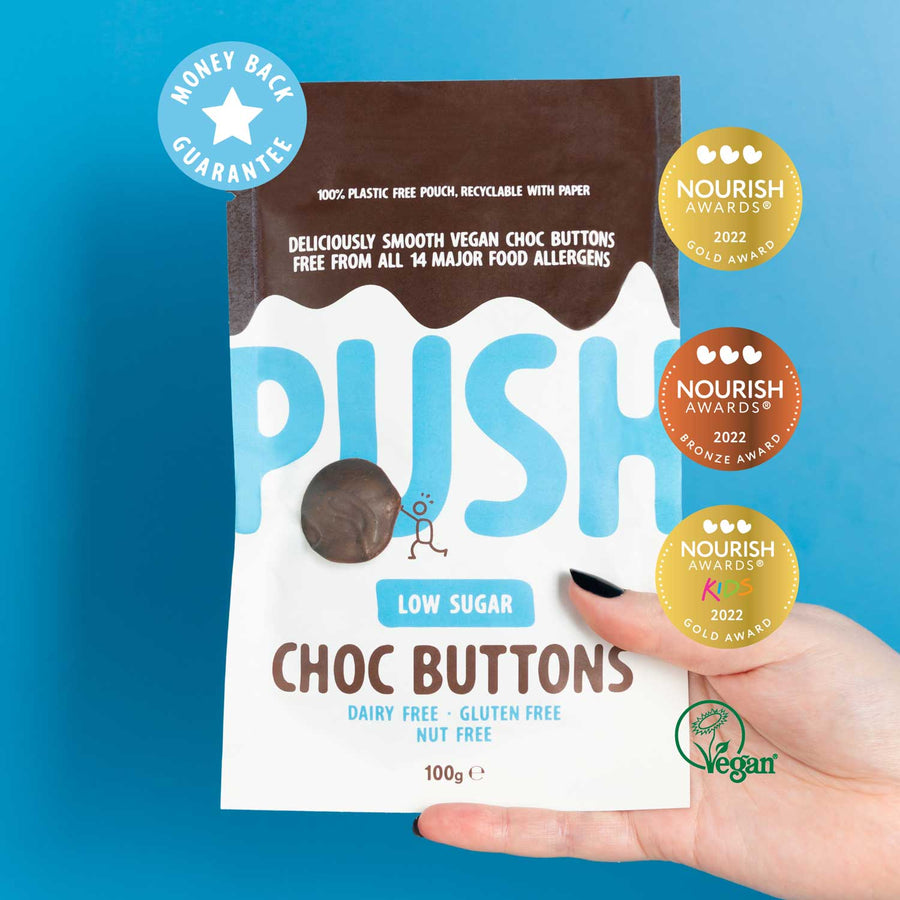 Holding a pouch of low sugar chocolate buttons with awards and vegan certification badge. 