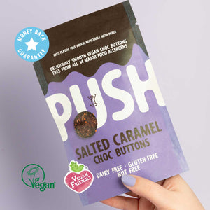 Holding a pouch of Push dairy free chocolate buttons with vegan certification. 