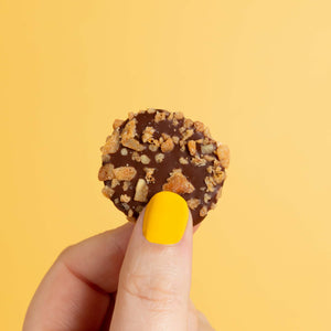 Close up of a honeycomb vegan chocolate button in front of a yellow backdrop.