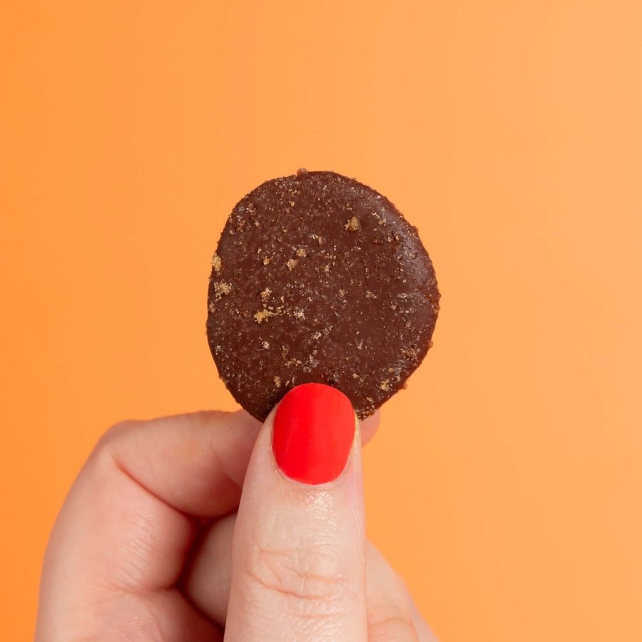 Orange dairy-free chocolate button held in front of orange backdrop.